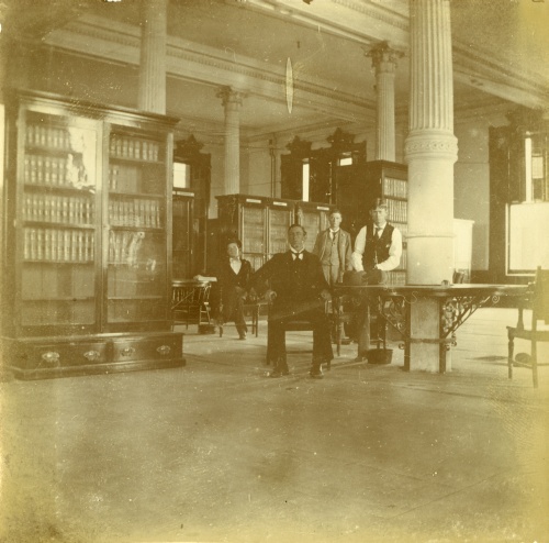 Image of the Supreme Court Library ca. 1897, a large room with high ceilings supported by columns, and containing large wooden desks and bookcases.